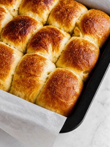 Golden brown, freshly baked Barley Malt Pull-Apart Loaves in a black baking pan lined with parchment paper, resting on a light marble surface.