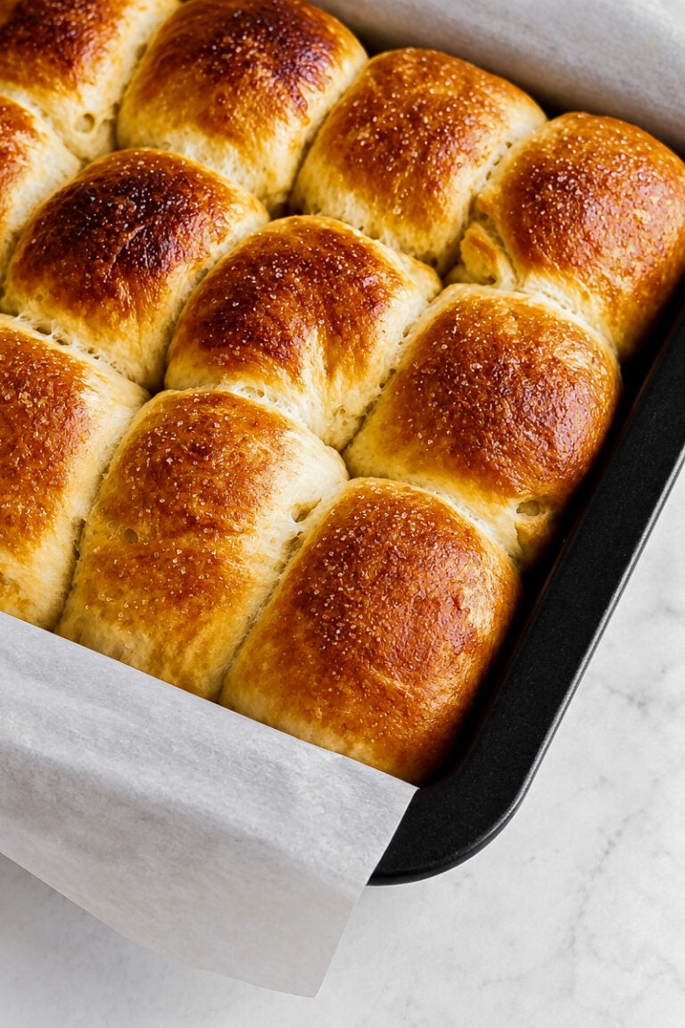 Golden brown, freshly baked Barley Malt Pull-Apart Loaves in a black baking pan lined with parchment paper, resting on a light marble surface.