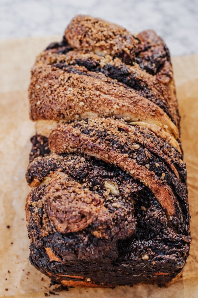A close-up of a freshly baked Chocolate Babka loaf with twisted layers of dough and chocolate filling, topped with a generous sprinkling of brown sugar.
