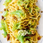Sicilian Pasta with Cauliflower: Spaghetti topped with green cauliflower florets, golden raisins, and crushed nuts on a white plate.