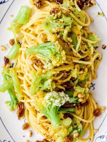 Sicilian Pasta with Cauliflower: Spaghetti topped with green cauliflower florets, golden raisins, and crushed nuts on a white plate.