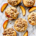 Close up of a peach streusel muffin split open showing juicy peach pieces inside the soft crumb.