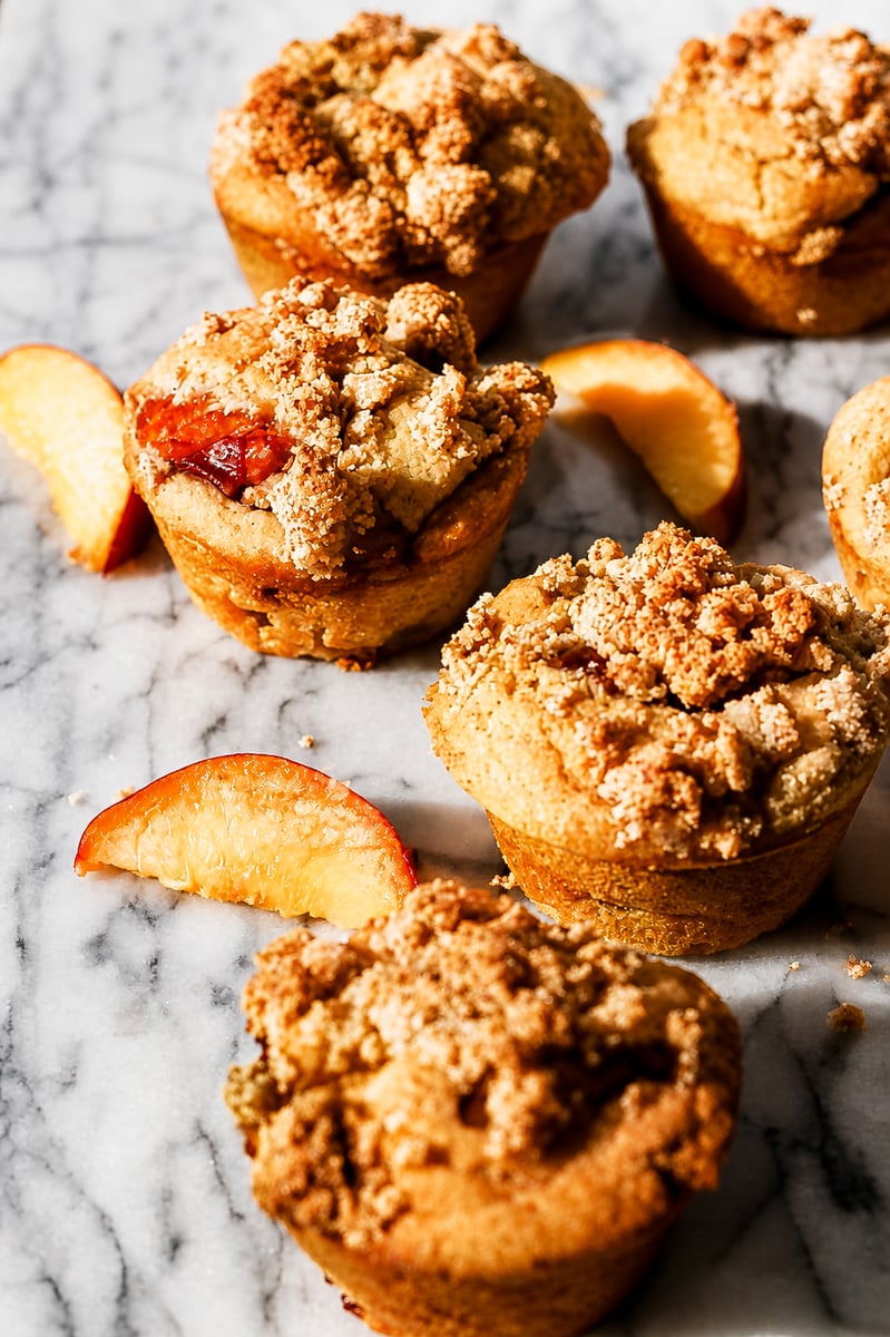 Close up of a peach streusel muffin split open showing juicy peach pieces inside the soft crumb