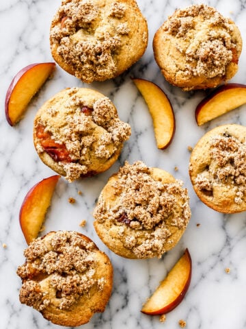 Close up of a peach streusel muffin split open showing juicy peach pieces inside the soft crumb.