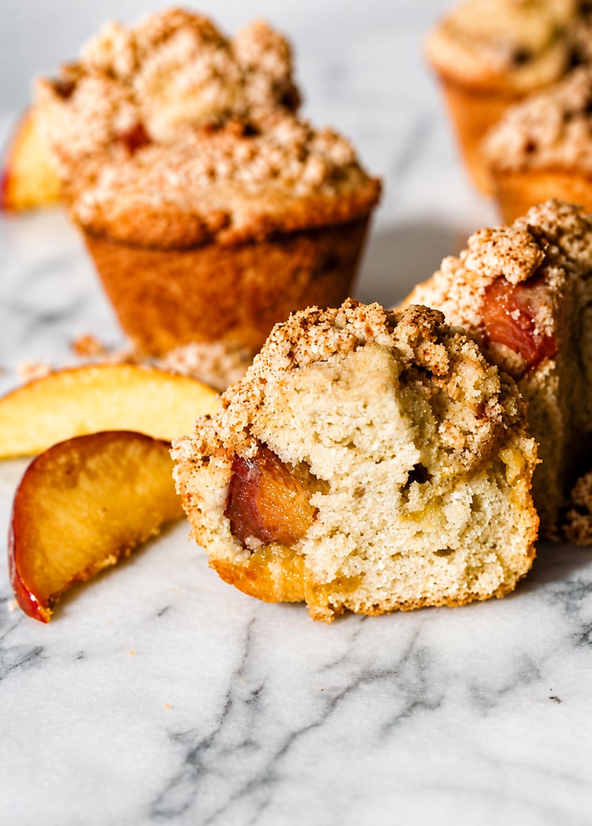 Close up of a peach streusel muffin split open showing juicy peach pieces inside the soft crumb