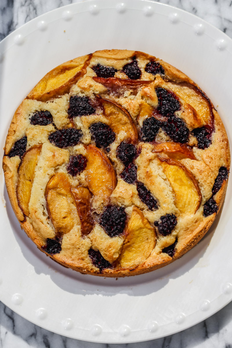 overhead image of a cake with peaches and blackberries on a white plate