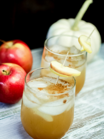 image of apple gin cocktail on wood board with apples in background