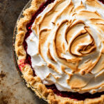 A cranberry meringue pie topped with toasted meringue in a glass pie dish.