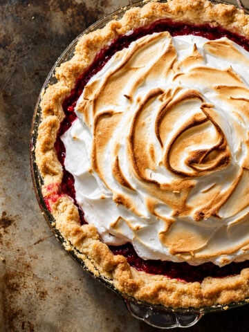 A cranberry meringue pie topped with toasted meringue in a glass pie dish.