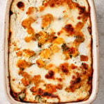 A baked casserole with a golden, bubbly cheese topping and visible chunks of vegetables in a rectangular dish, resting on a light countertop-this Roasted Butternut Squash and Pumpkin Lasagna is both comforting and vibrant.