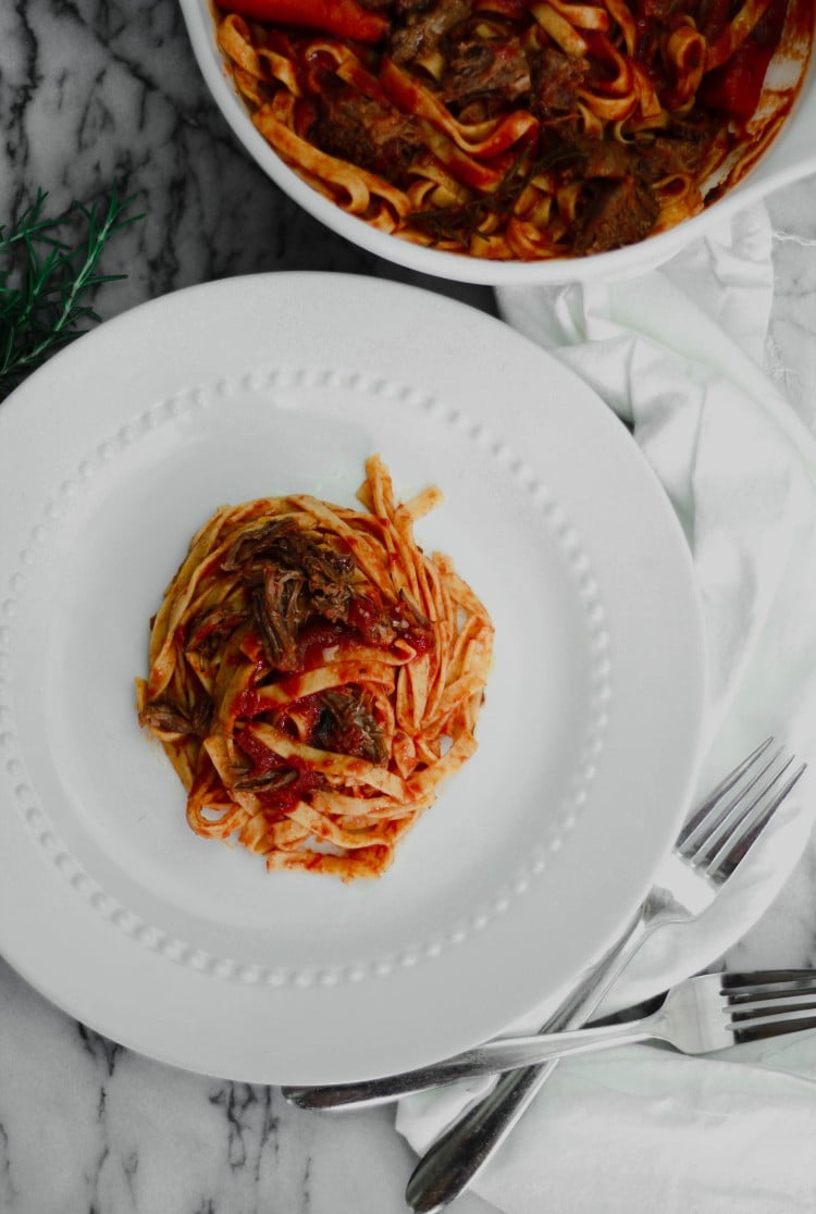 overhead image of pasta on a white plate with forks and napkin in background