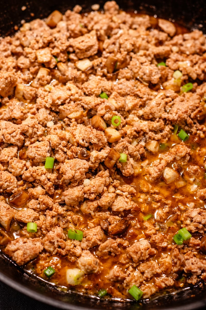 Ground meat cooked in a skillet with diced vegetables, green onions, and a savory brown sauce-perfect for chicken lettuce wraps. The mixture is well seasoned and finished with fresh chopped scallions.