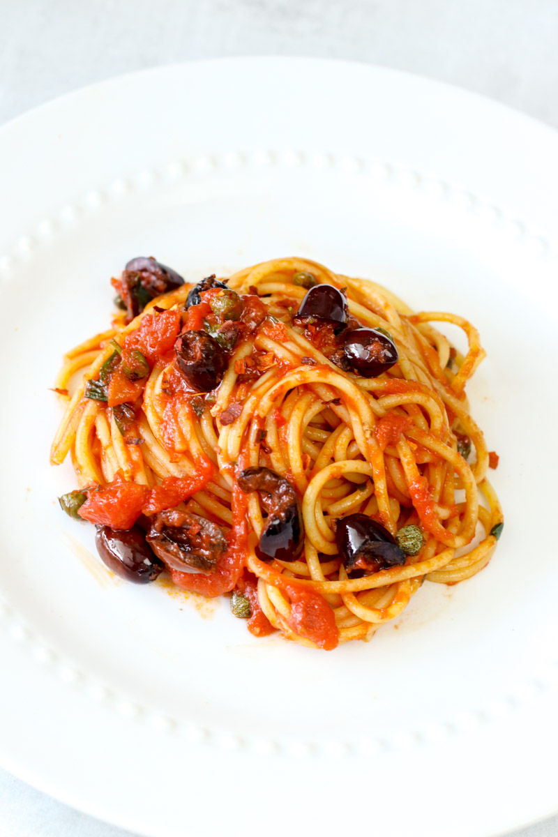 overhead image of easy pasta puttanesca on a white plate.