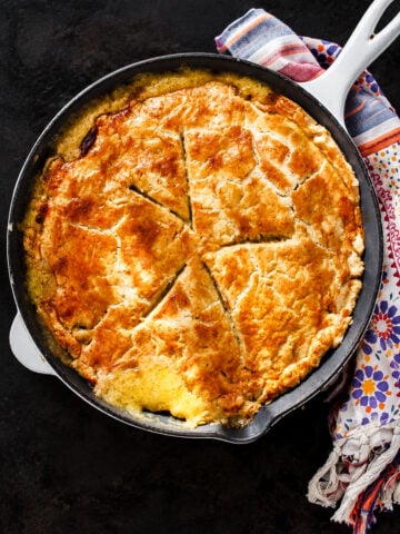 A golden-brown turkey pot pie with a sliced crust, served in a white enameled cast iron skillet on a dark surface.