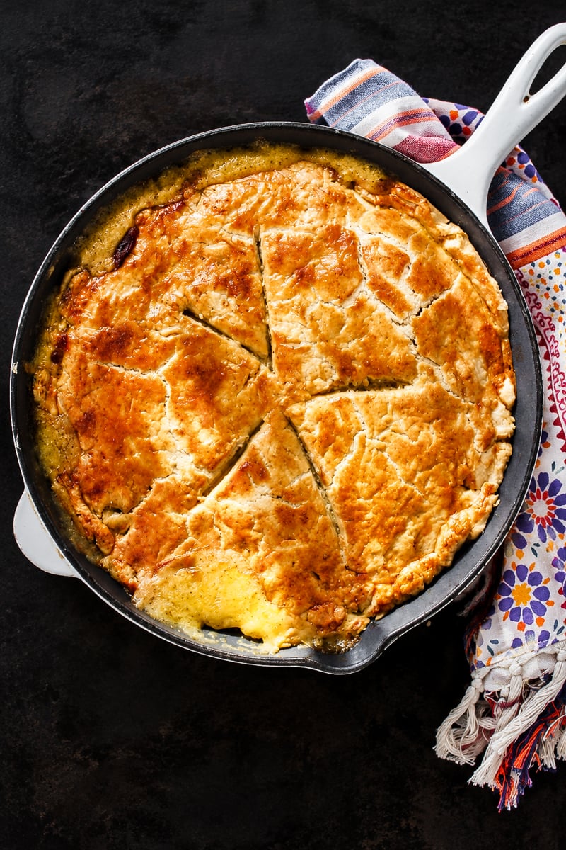 A golden-brown turkey pot pie with a sliced crust, served in a white enameled cast iron skillet on a dark surface.