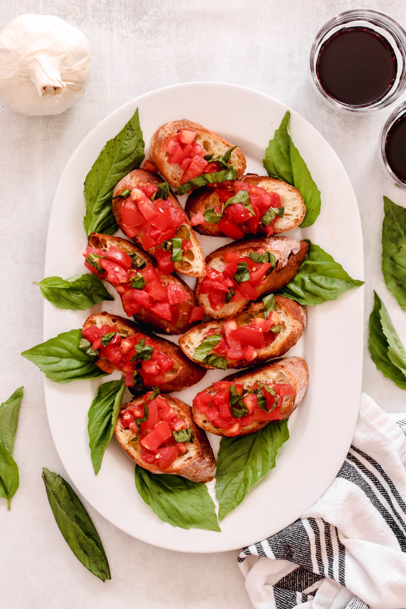 overhead image of bread slices topped with tomatoes, garlic and basil in the background.