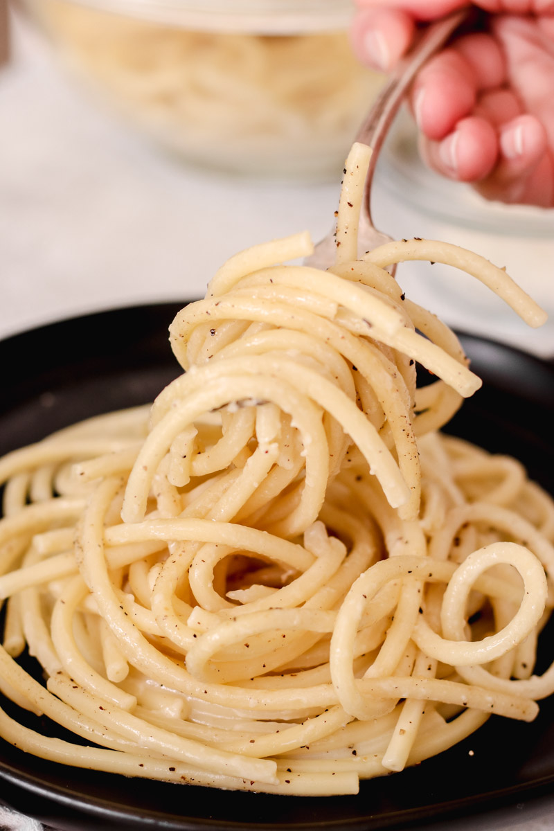 closeup image of pasta on a black plate being picked up by a hand and a fork. 