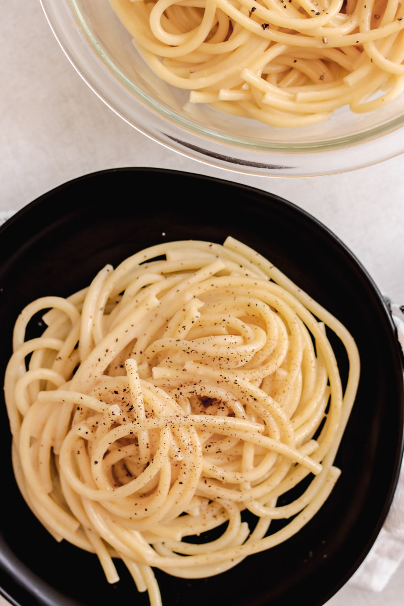 overhead image of pasta on a black plate and a glass bowl with more pasta.