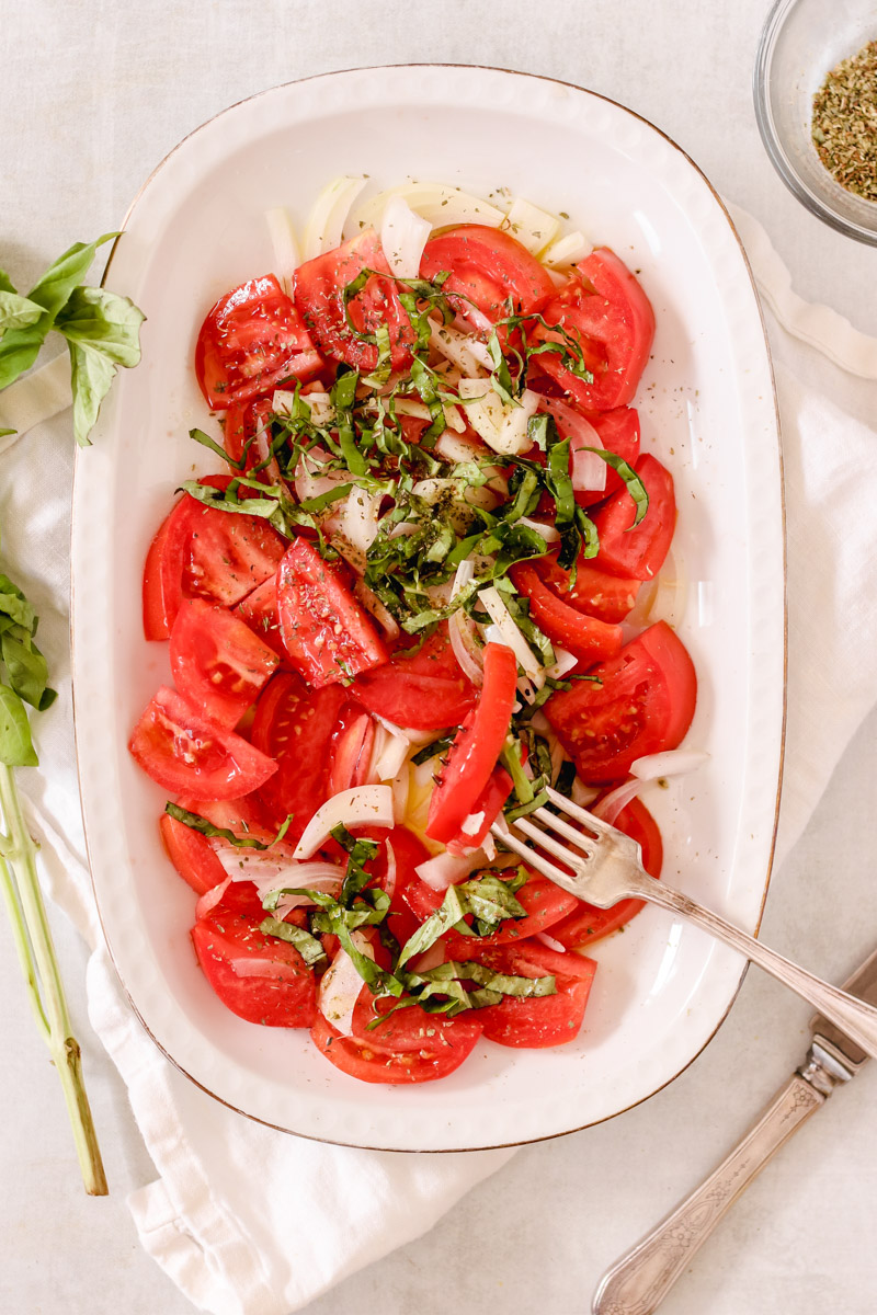 overhead image of a tomato and onion salad in a white plate with a fork.