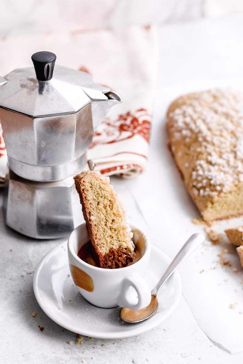 image of baked good dipped into an espresso cup and a coffee maker in the background.