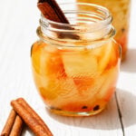 Glass jar of pickled watermelon rind with cinnamon stick on a wooden surface