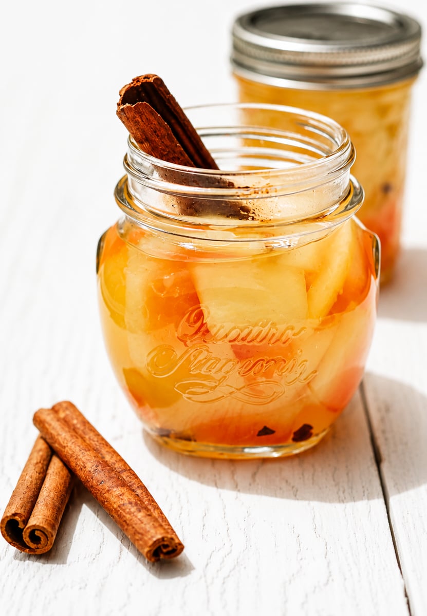 Glass jar of pickled watermelon rind with cinnamon stick on a wooden surface