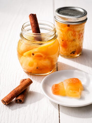 Glass jar of pickled watermelon rind with cinnamon stick on a wooden surface
