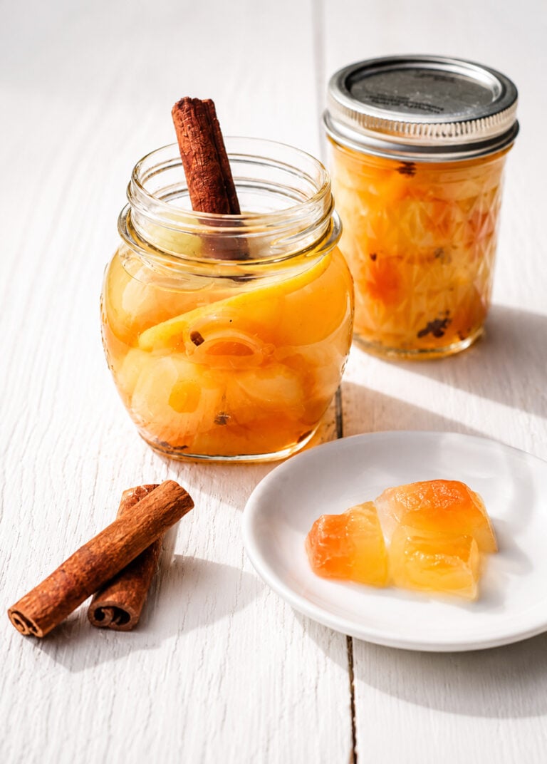 Glass jar of pickled watermelon rind with cinnamon stick on a wooden surface