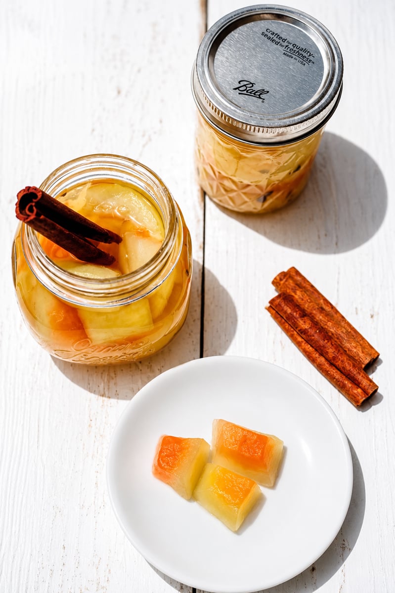 Glass jar of pickled watermelon rind with cinnamon stick on a wooden surface