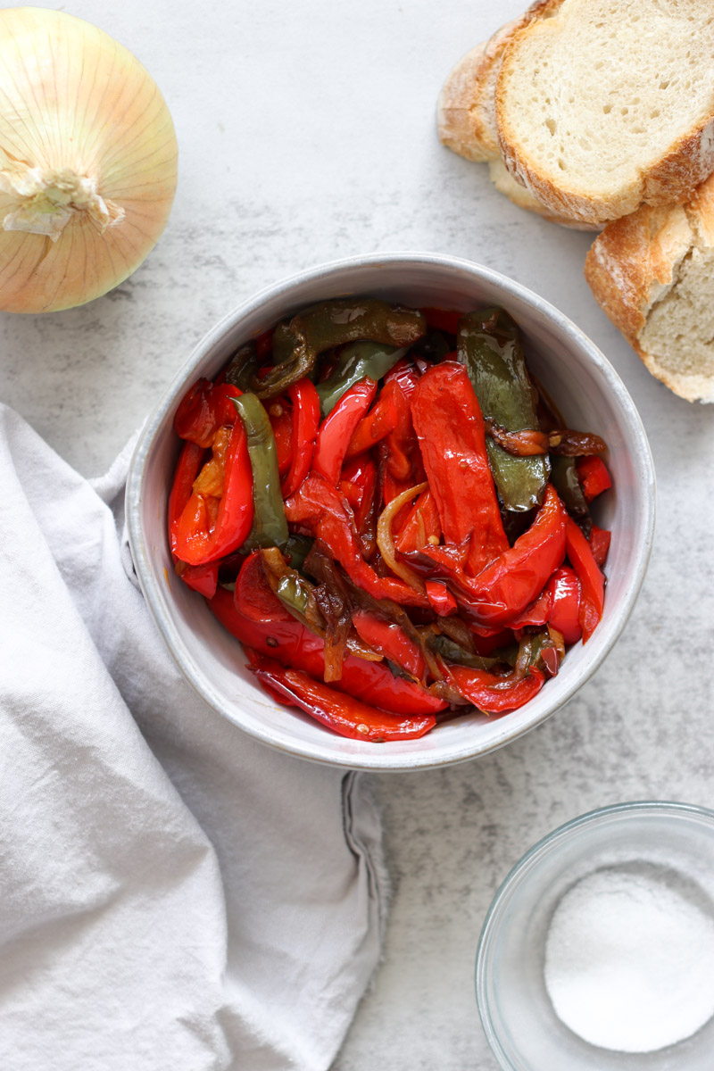image of red and green peppers in a white bowl, onion and bread slices in background.