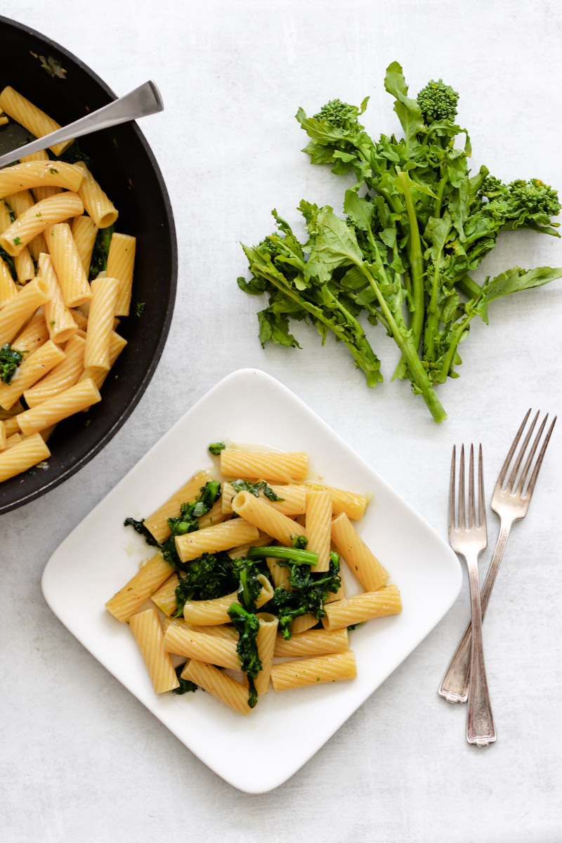image of pasta with rapini on white plate and forks and rapini in background.
