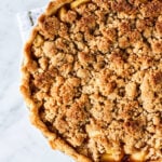 An apple crumble pie with oat streusel and a flaky crust in a white ceramic dish.