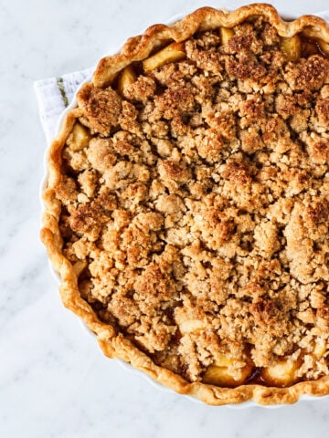 An apple crumble pie with oat streusel and a flaky crust in a white ceramic dish.