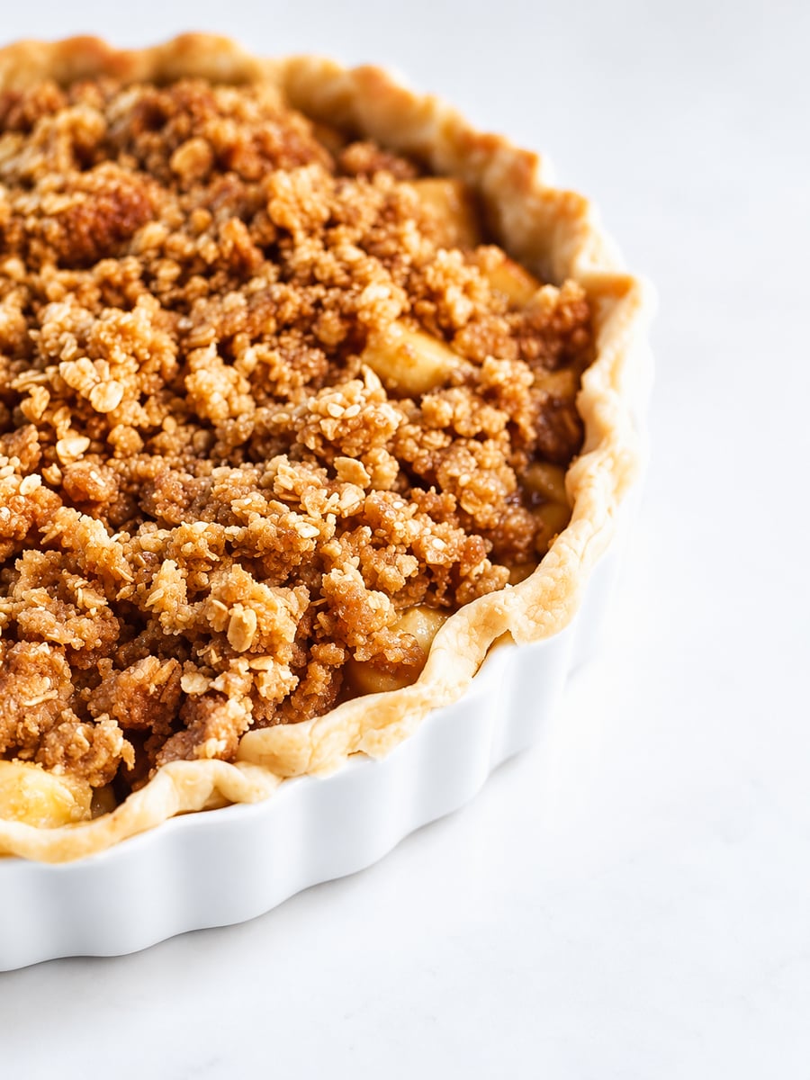 Apple pie with oat streusel in a white ceramic dish, topped with a golden brown oat crumble.