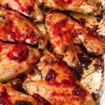 Baked chicken wings on a foil-lined tray, topped with a bright red cranberry sauce, with areas of slight charring and caramelization visible-reminiscent of the deep flavors found in slow roasted turkey wings.