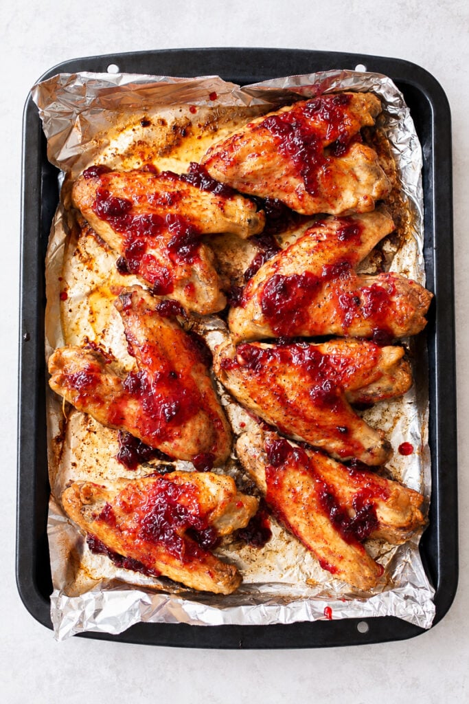 Baked chicken wings on a foil-lined tray, topped with a glossy red sauce and arranged neatly in rows, evoke the mouthwatering appeal of slow roasted turkey wings with their savory aroma and perfectly tender texture.