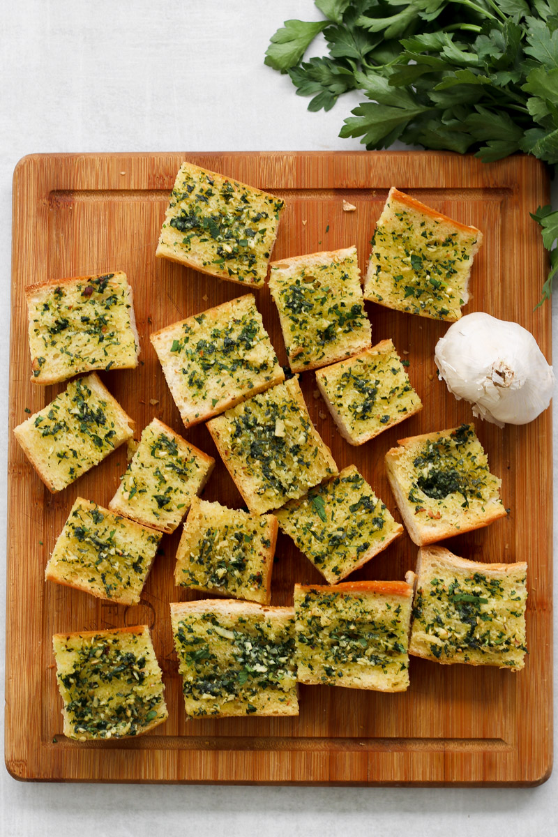 overhead image of chunks of garlic bread on a wooden serving board.