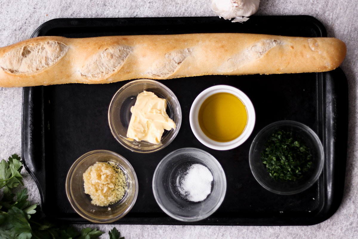 overhead image of ingredients to make garlic bread on a baking sheet. 