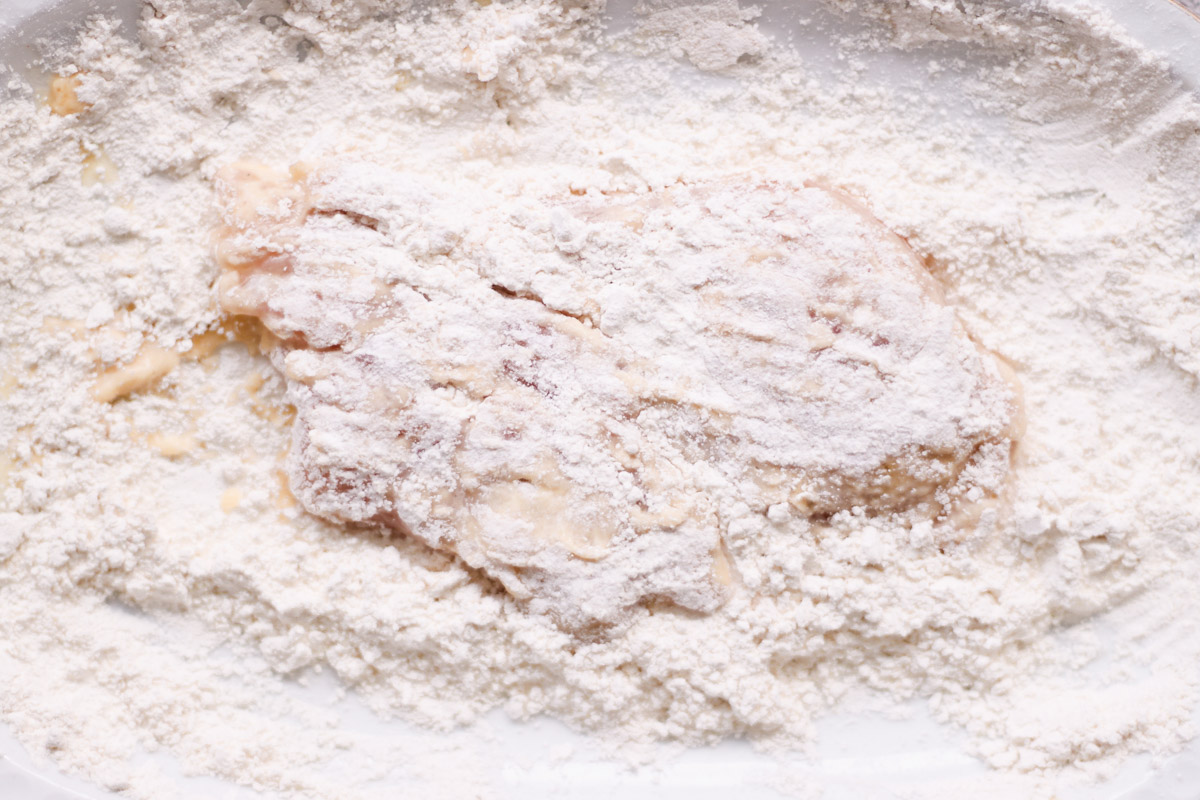 overhead image of dredging chicken breasts in flour. 