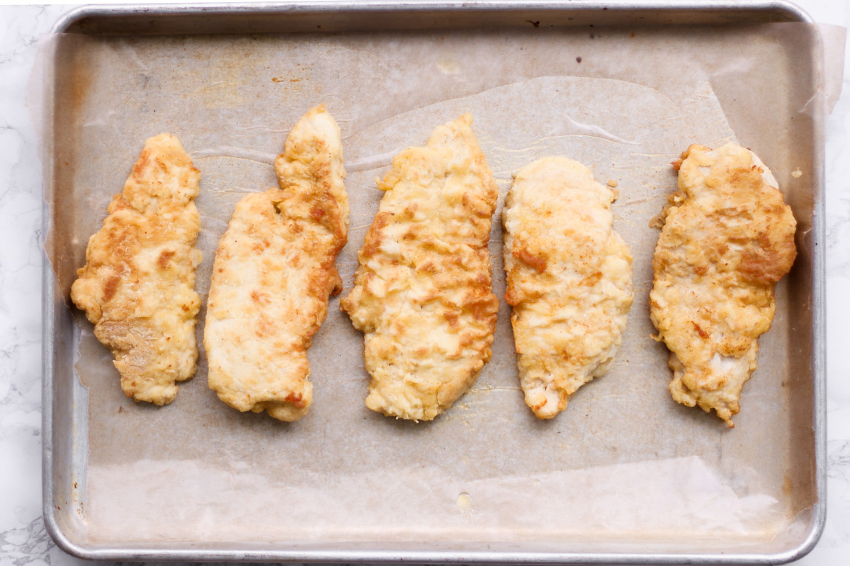 overhead image of pan fried chicken breasts on a baking sheet. 
