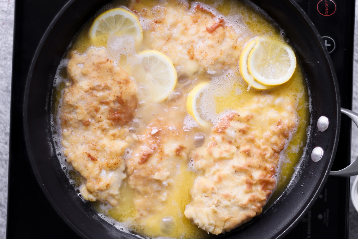 overhead image of chicken simmering in a lemon butter sauce. 
