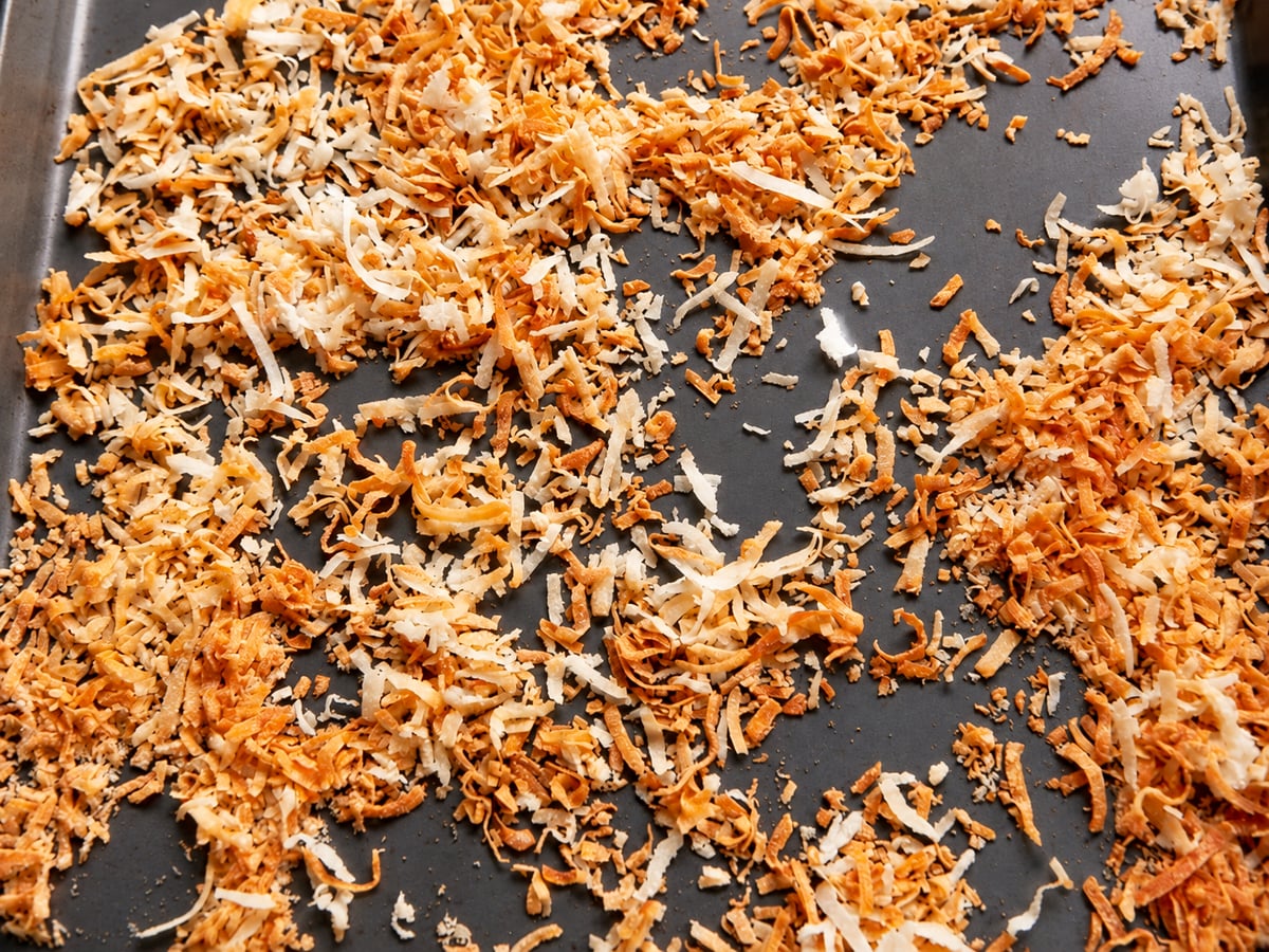 Golden brown toasted shredded coconut on a dark baking sheet, perfect for topping a pumpkin cake.