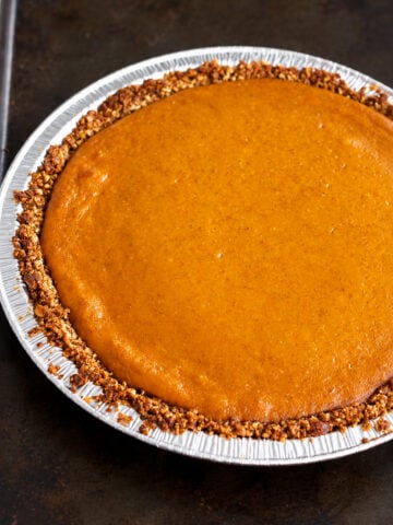 A gluten-free pumpkin pie with a nut-crusted edge in a disposable aluminum pan.