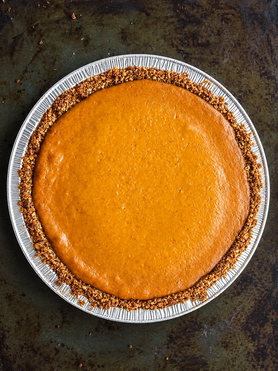 A whole gluten-free pumpkin pie with a crunchy nut-like crust in a round aluminum pan.