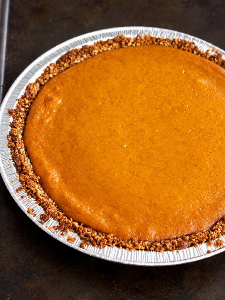 A gluten-free pumpkin pie with a nut-crusted edge in a disposable aluminum pan.