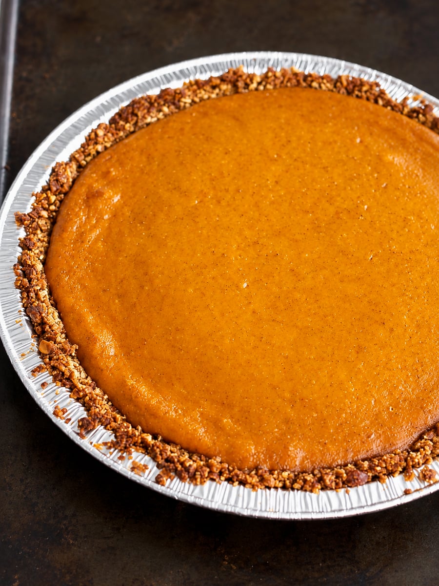 A gluten-free pumpkin pie with a nut-crusted edge in a disposable aluminum pan.