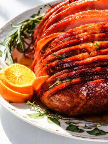 A spiral ham recipe centerpiece featuring a glazed, spiral-sliced ham garnished with fresh herbs and orange slices on a serving platter.