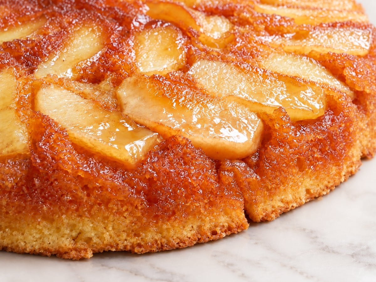Close-up of a golden brown Apple Upside-Down Cake with caramelized apple slices glistening on top, set on a white marble surface.