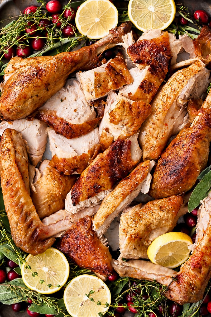 Roast turkey pieces are artfully arranged on a platter with fresh lemon slices, cranberries, and aromatic herbs like sage and thyme for garnish.