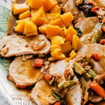 Sliced Roast Pork Tenderloin with Butternut Squash, accompanied by carrots, celery, and chunks of cooked yellow squash on a decorative plate, all topped with savory brown sauce.